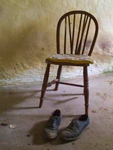 empty chair with man's old shoes in a stone room.
